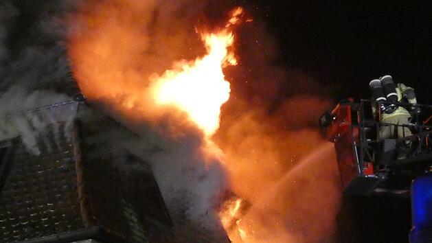 Die Flammen schlagen aus dem Dach, die Feuerwehr l&ouml;scht &uuml;ber die Drehleiter, nachdem sie die Bewohner gerettet hat.