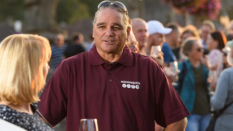 Br&uuml;ckenw&auml;chter David Obermeier spricht auf der alten Mainbr&uuml;cke mit G&auml;sten. Seit der Einf&uuml;hrung des sogenannten "Br&uuml;ckenschoppens" genie&szlig;en  bei sch&ouml;nem Wetter zahlreiche Menschen auf der Br&uuml;cke den sch&ouml;nen Ausblick und ein Glas Wein.  Foto: Daniel Peter/dpa