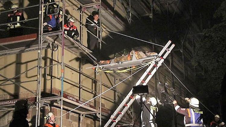 Mit  Leiter und Seilen wird der Verletzte in waagerechter Position auf der Trage vom Baugerüst abgelassen.