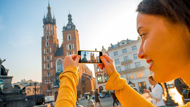 Young smiling female traveler photographing St. Marys Basilica with mobile phone on the sunrise in Krakow Junge lächelnde Reisende, die die St. Marien-Basilika mit dem Handy bei Sonnenaufgang in Krakau fotografiert
