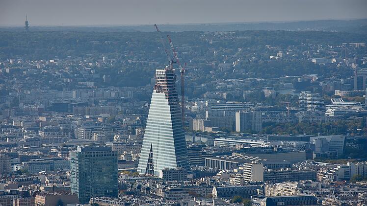 Panoramablick auf Paris vom Montparnasse-Turm mit dem im Bau befindlichen Tour Triangle, der sich vom traditionellen Stadtbild abhebt.  From the top of the Montparnasse Tower, a panoramic view of Paris unfolds, where the still-under-construction Triangle Tower stands out with its pyramidal silhouette amidst the traditional rooftops of the 15th arrondissement. The contrast between contemporary architecture and the classic urban fabric reflects the city's visual and cultural transformation. Ideal for tourism, editorial, and cultural content on urban planning, modern architecture, and metropolitan evolution