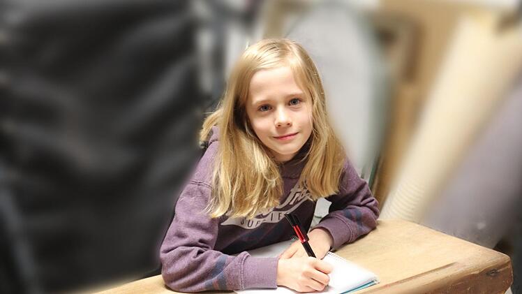 Fenja probiert die alte Schulbank aus und findet sie hart, unbequem und man sitzt so richtig eng und eingepfercht. Foto: Johanna Blum