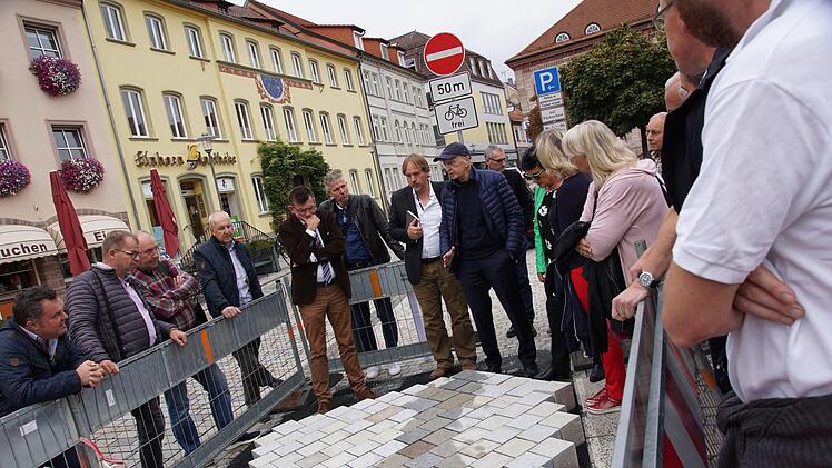 Bürgermeister Armin Warmuth, Stadtbaumeister Detlef Mohr und Architekt Hartmut Holl beugen sich mit den Stadträten über die Musterpflasterfläche am Marktplatz. Foto: Arkadius Guzy