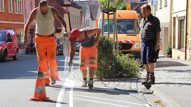 Werner Grell vom Bauhof der Stadt Ebern (rechts) wacht darüber, dass Uwe Kischel und Nico Langbein (Mitte) die Streifen richtig positionieren. Mit Sprühfarbe markieren die Arbeiter die "Eingangsportale" zur verkehrberuhigten Zone auf der Fahrbahn. Foto: Eckehard Kiesewetter