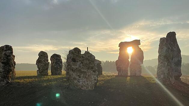 Steinkreis in der Fr&auml;nkischen Schweiz bei Sonnenuntergang, erinnert an Stonehenge. Die Steine stehen auf einem Feld, die Sonne scheint durch die L&uuml;cken, was eine mystische Atmosph&auml;re schafft.