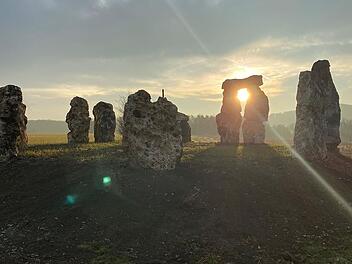 Steinkreis in der Fr&auml;nkischen Schweiz bei Sonnenuntergang, erinnert an Stonehenge. Die Steine stehen auf einem Feld, die Sonne scheint durch die L&uuml;cken, was eine mystische Atmosph&auml;re schafft.