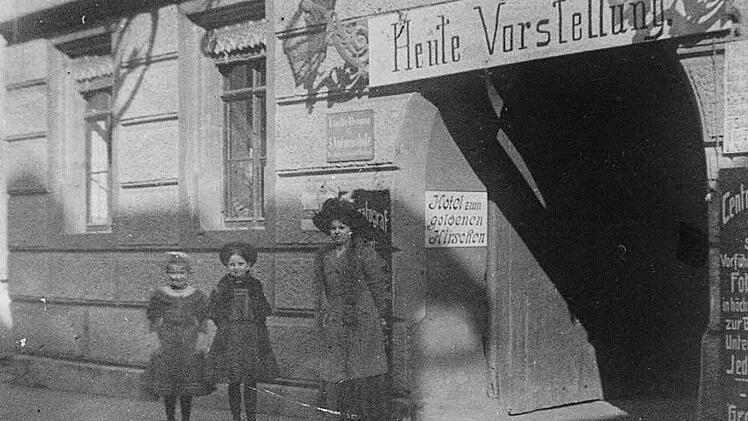 Eingang zum ersten Kino Kulmbachs im Jahr 1909: Durch das Tor des Hotels "Zum goldenen Hirschen" in der Langgasse 12 gelangt der Besucher in den Vorführraum, der 350 Personen Platz bietet. Wie eine Tafel links oben ausweist, dient der Innenhof auch als "Einstellraum für 5 Automobile". Rechts vom Torbogen wird das aktuelle Programm inseriert. Nach dem Ersten Weltkrieg wird der "Goldene Hirsch" in ein Kaffeehaus (Café Beyerlein) umgebaut. Das 1911 in die Langgasse 14 verlegte "Central-Theater" ...