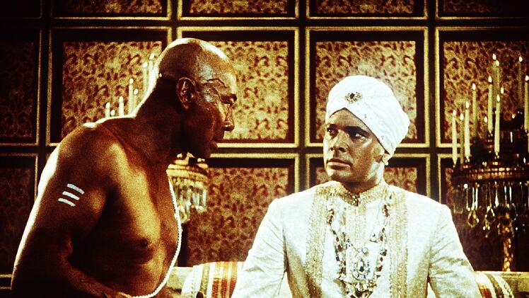 Der Oberpriester will den Maharadscha Chandra (Walther Reyer, rechts) zu einem gefährlichen Gottesurteil drängen.