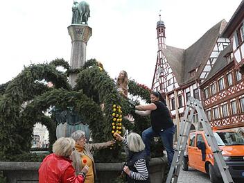 Während von unten die Gästeführerinnen Marlene Hahn, Ingeborg Oelschner und Ulli Baier (v.l.) Regieanweisungen geben, stecken die Gartenamtsmitarbeiterinnen Anke Schönbrodt (r.) und Eva Giesel (oben) von der Leiter aus die rot-gelben Eier an den Osterbrunnen.  Foto. Barbara Herbst