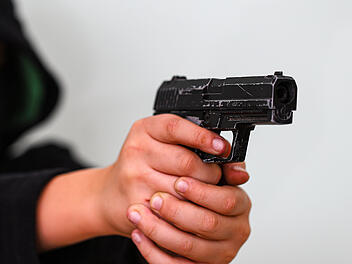 Ein vermummter junger Mann in Schwarz zielt mit einer Pistole. Konzept von Kriminalität und Schusswaffenangriff mit jungem Mann. Bewaffneter Raubüberfall