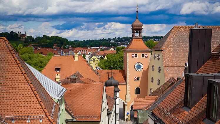 Malerische Altstadt mit roten Ziegeld&auml;chern und einem markanten Uhrturm. Die Architektur und die gr&uuml;ne Landschaft im Hintergrund verleihen dem Bild eine idyllische Atmosph&auml;re.