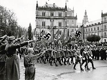 "Vorbeimarsch der SA mit Fahnen bei der Feier der 20. Wiederkehr des Deutschen Tages von 1922 auf dem Schlossplatz im Jahr 1942" lautet die Beschreibung dieses Fotos aus dem Staatsarchiv Coburg. Am 14./15. Oktober 1922 war die SA erstmals massenhaft in Coburg aufmarschiert. Sie reiste mit 650 Mann zum "Deutschen Tag" des "Schutz- und Trutzbunds" an, angeführt von Adolf Hitler. Aufnahme: Leo Bauer, Gau-Archiv Bayerische Ostmark der NSDAP. Bildquelle: Staatsarchiv Coburg, Bildsammlung 6_9-504