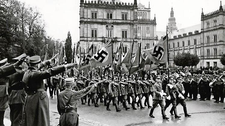 "Vorbeimarsch der SA mit Fahnen bei der Feier der 20. Wiederkehr des Deutschen Tages von 1922 auf dem Schlossplatz im Jahr 1942" lautet die Beschreibung dieses Fotos aus dem Staatsarchiv Coburg. Am 14./15. Oktober 1922 war die SA erstmals massenhaft in Coburg aufmarschiert. Sie reiste mit 650 Mann zum "Deutschen Tag" des "Schutz- und Trutzbunds" an, angeführt von Adolf Hitler. Aufnahme: Leo Bauer, Gau-Archiv Bayerische Ostmark der NSDAP. Bildquelle: Staatsarchiv Coburg, Bildsammlung 6_9-504