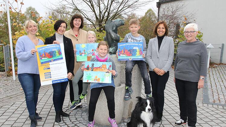 Das "Veste-Bild" von Felix Meyer ziert in diesem Jahr den Adventskalender des Lions Club Coburg Veste. V. l.: Sonja Erdel,  Ingrid Nassios, Präsidentin Lions-Club Coburg Veste,Gabriele Gruschwitz, Marie Schneider, Marlene Schneider, Felix Meyer, Schulleiterin Karina Kräußlein-Leib und Konrektorin Angelika Geiß-Dekrell mit Schulhund "Ricky". Desombre