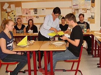 "Knigge-Trainerin Yasmin Birk (Mitte) beim Thema Tischmanieren mit Mona (links) und Kevin am Tisch beim Umgang mit der Serviette. Foto: gg