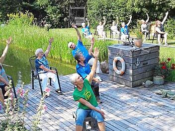 Morgenyoga am Teich kann im Sitzen und im Stehen ausgeführt werden, wichtig sind die Bewegung und der Spaß, sagt Trainerin Birgit Schmitt (vorne im grünen T- Shirt).  Foto: K.- H. Hofmann