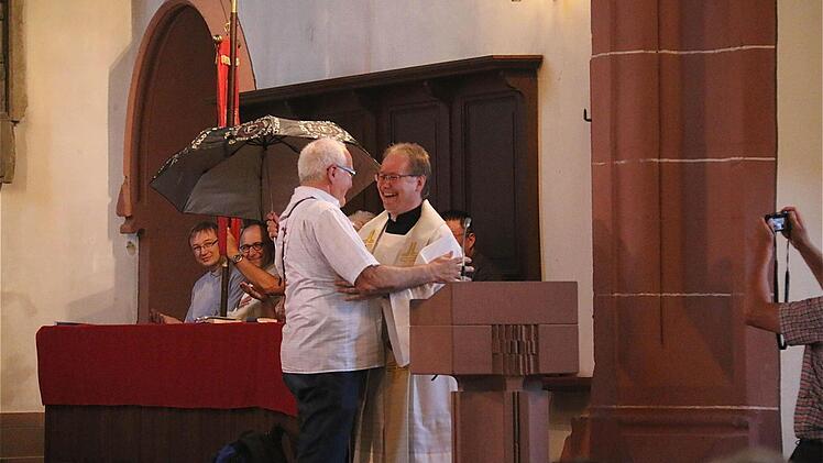 Gerhard Dehler (links), Leiter der Walldürn-Wallfahrer, schenkt Pfarrer Thomas Eschenbacher einen Regenschirm.