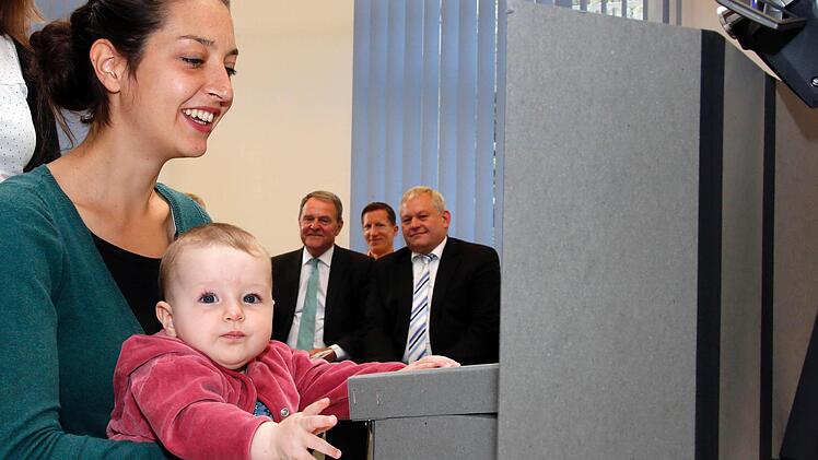 NEPS-Mitarbeiterin Kerstin Hoenig demonstrierte am Donnerstag mit ihrer Tochter Ida Marlen, wie Babys für das Nationale Bildungspanel getestet werden. Auch der bayerische Wissenschaftsminister Wolfgang Heubisch (hinten links) schaute zu. Foto: Matthias Hoch
