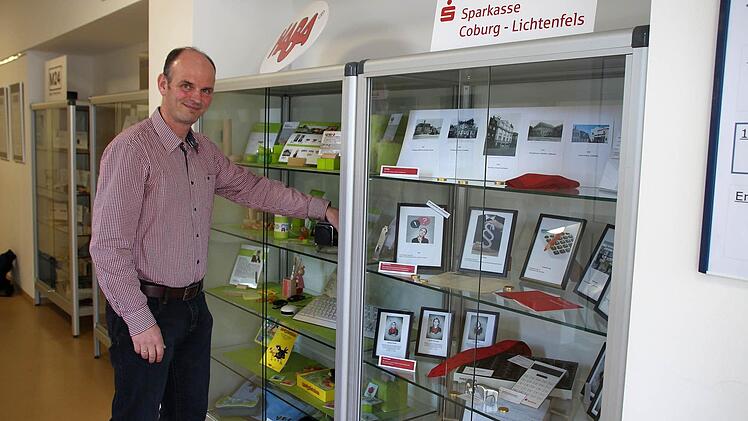 Wirtschaftslehrer Stefan Kestel zeigt die Vitrinen im ersten Stock des Gymnasiums Ernestinum. Hier präsentieren sechs heimische Unternehmen ihre Geschichte und informieren unter anderem über Produktionsabläufe und Ausbildungsmöglichkeiten. Foto: Ulrike Nauer