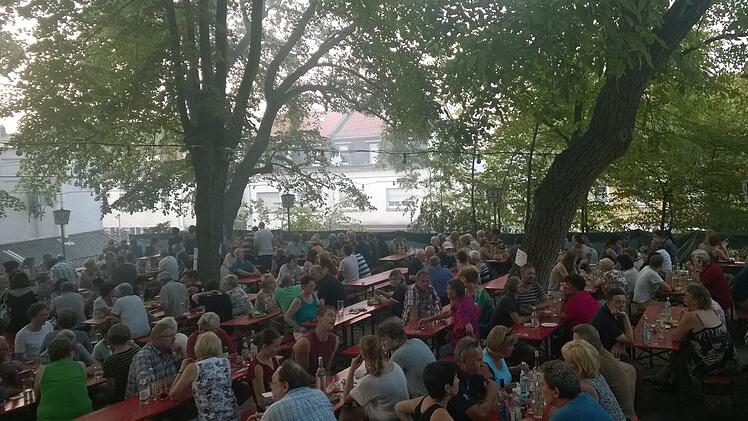 Der Portugiesische Volksgarten in Bamberg-Gaustadt zeigt viele Menschen, die an Tischen unter Bäumen sitzen und sich unterhalten. Eine gemütliche Atmosphäre im Freien.