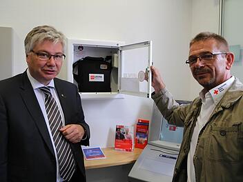 Kemmerns Bürgermeister Rüdiger Gerst (links) mit Thomas Stemper vom BRK-Kreisverband Bamberg bei der Installation des Defibrillators in der Sparkasse.  Foto: Sebastian Martin