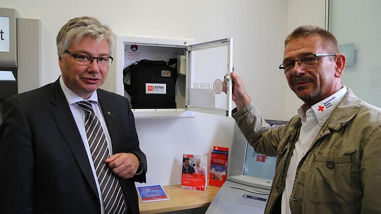 Kemmerns Bürgermeister Rüdiger Gerst (links) mit Thomas Stemper vom BRK-Kreisverband Bamberg bei der Installation des Defibrillators in der Sparkasse.  Foto: Sebastian Martin