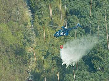 Ein Hubschrauber der Bundespolizei wirft am Donnerstag über einem Wald bei Reupelsdorf Wasser ab. Foto: Tobias Köpplinger