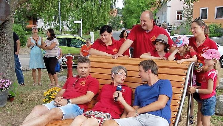 Die neue Gartenliege auf dem Meedensdorfer Brunnenplatz gefiel auch dem Team vom Bayerischen Rundfunk. Im Bild Redakteur Moritz Pompl auf der Liege im Gespräch mit Christel Klötzscher, der Sponsoren-Beauftragten der "Herzplatz"-Aktion. Foto: Andrea Spörlein