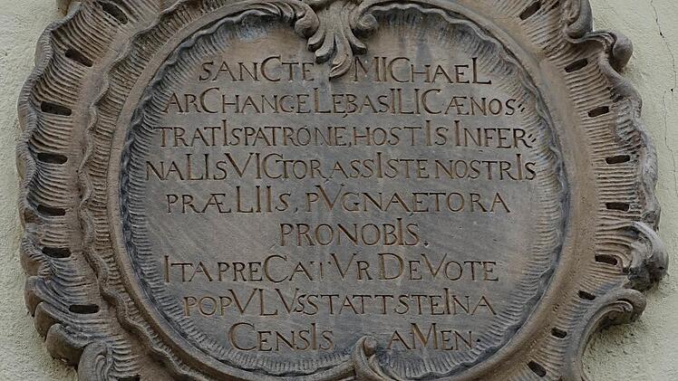 Der Gedenkstein über den nördlichen Eingang der Pfarrkirche enthält ein Bittgebet an den Schutzpatron St. Michael und ein verstecktes Chronogramm, das zu entschlüsseln war.