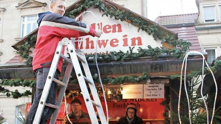 Die Bäckerei Möckel baut ihren Stand seit 1978 auf dem Weihnachtsmarkt auf: Christian Möckel (auf der Leiter) bringt noch eine Lichterkette an, während Ursula Möckel die Tassen für den Glühwein einräumt. Hilfe bekommen sie von Klaus Dragon.  Fotos: Thomas Heuchling