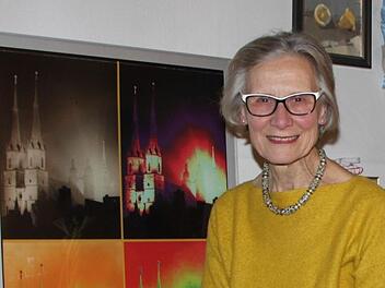 Adelheid Zimmermann sitzt vor einer Collage, die sie aus Fotografien ihres Vaters angefertigt hat. Sie zeigen dessen Heimatstadt Halle. Foto: Ulrike Müller