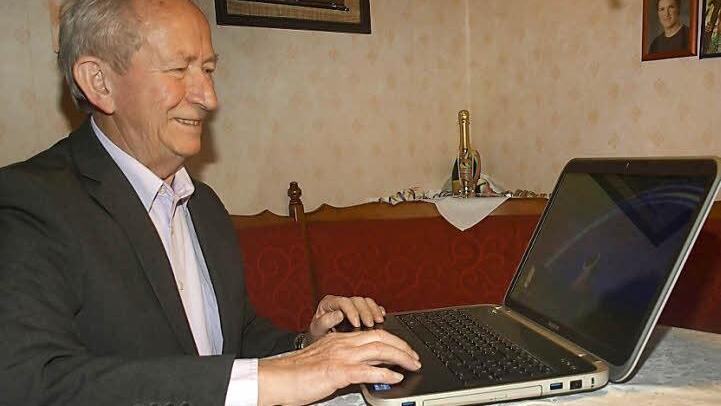 Siegfried Albert aus Ebenhausen mit Laptop und Saale-Zeitung: Der langjährige Kommunalpolitiker feiert am 12. Januar seinen 75. Geburtstag. Foto: Stefan Geiger