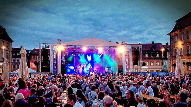 Ein lebhaftes Sommerfestival in Bamberg: Menschen versammeln sich vor einer B&uuml;hne mit buntem Licht. &Uuml;ber 60 Bands sorgen f&uuml;r eine gro&szlig;artige Atmosph&auml;re beim Blues- & Jazzfestival.