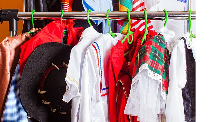 Ein bunter Kleiderständer voller Faschingskostüme in verschiedenen Farben, darunter rote, karierte und gestreifte Muster, erinnert an das traditionelle "Kaufhaus der fünf Jahreszeiten".