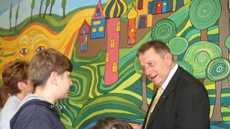 Oberbürgermeister Henry Schramm lässt sich von den kleinen Künstlern selbst das riesige Wandgemälde erklären. Auf dem Wandgemälde sind kunterbunte Häuser mit witzigen Dächern, ein Wald, aber auch eine fröhliche Sonne zu sehen. Foto: Sonny Adam