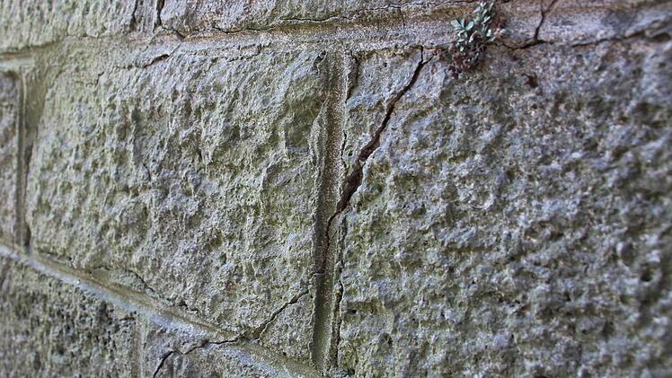 Risse zeigen sich in der alten Brückenmauer aus Naturstein.