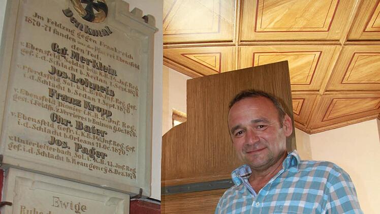 Hubert Reuß vom Bauamt der Gemeinde Ebensfeld steht an der Stelle neben der Eingangstür, wo ein sogenanntes Befundfenster zu sehen ist. Es zeigt die ursprüngliche Schicht der anhand dessen rekonstruierten Wandfarbe.