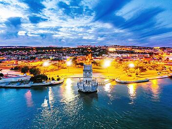 Lisbon, Portugal. Aerial view of Belem Tower in Lisbon, Portugal during the sunset. Illuminated buildings with cloudy sky and ocean. Lissabon, Portugal. Luftaufnahme des Belem-Turms in Lissabon, Portugal, während des Sonnenuntergangs. Beleuchtete Gebäude mit bewölktem Himmel und Meer. Luftaufnahme des Belem-Turms in Lissabon, Portugal, während des Sonnenuntergangs