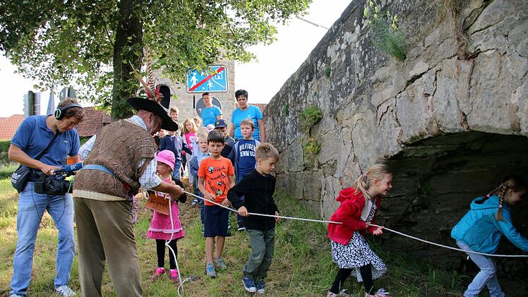 Die Kinder halten sich an einem Seil fest, während sie unter der Rodachbrücke durchkriechen. Foto: Bettina Knauth