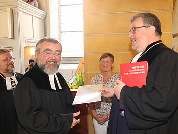Dekan Christoph Liebst überreicht die Urkunde für die Pfarrstelle an Pfarrer Wolfgang Leikert (links). Foto: Michael Stelzner