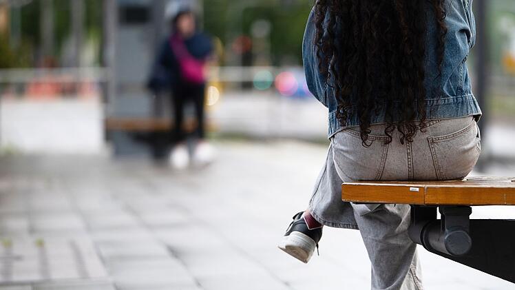 Eine junge Frau sitzt an einer Haltestelle auf einer Bank