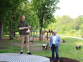 Jugendreferent Adrian Bier testet im Beisein von Bürgermeister Michael Kastl die neue Drehscheibe auf dem Jörgentorspielplatz. Im Hintergrund sind Kinder auf dem neuen Klettergerüst zu sehen. Foto: Thomas Malz