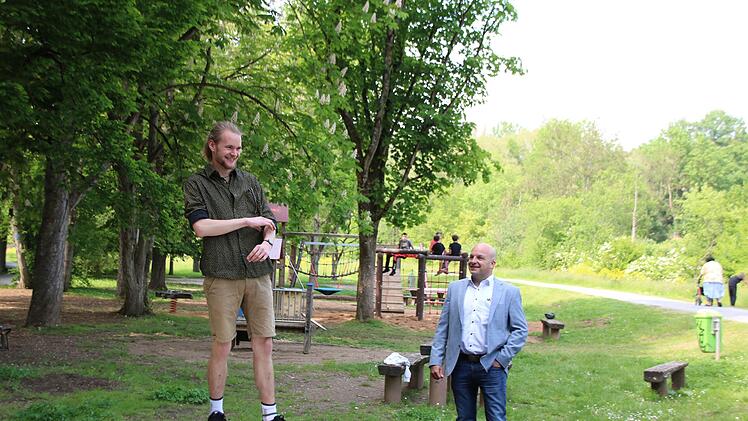 Jugendreferent Adrian Bier testet im Beisein von Bürgermeister Michael Kastl die neue Drehscheibe auf dem Jörgentorspielplatz. Im Hintergrund sind Kinder auf dem neuen Klettergerüst zu sehen. Foto: Thomas Malz