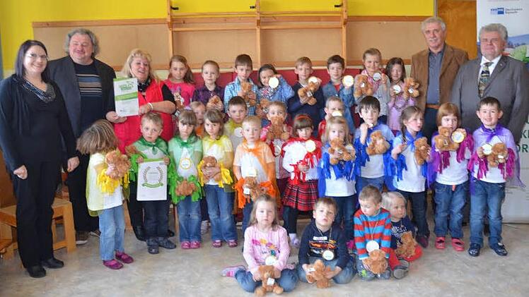 Die Kinder vom Kindergarten Gundelsdorf sind stolz auf ihr Zertifikat "Haus der kleinen Forscher" und zeigen die Teddybären und Medaillen, die es als Belohnung für die kleinen Forscher gab. Mit im Bild von links Andrea Wild (IHK), Pater Waldemar Brysch, Birgit Eisentraudt (Leitung Kindertagesstätte), und (von rechts) Fred Wunder (IHK) und Dritter Bürgermeister Hans Simon Foto: Karl-Heinz Hofmann