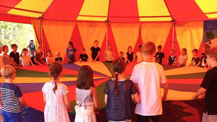 Ein buntes Zelt mit spielenden Kindern unter einem farbenfrohen Tuch. Der Ort wirkt einladend und fröhlich, mit Raum für Lernen und Gemeinschaft.