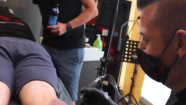 Sponsor Hans-G&uuml;nter Wirth (Mitte) beobachtet wie Marcus Fleischmann das Tattoo sticht.  Foto: Johanna Blum