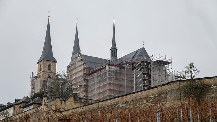 Die Bamberger Klosterkirche St. Michael ist eingerüstet, während die Sanierungsarbeiten andauern. Im Vordergrund sieht man Weinreben.