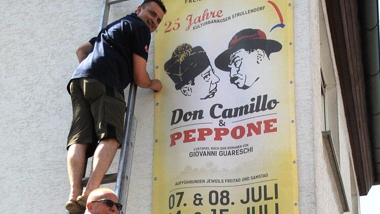 Bläcky Schwarzmann (unten) und Stefan Wagner, zwei "Kulturbanausen", die nicht auf der Bühne stehen, aber organisatorisch in vorderster Front aktiv sind, befestigen in der Bamberger Straße, nur einen Steinwurf von der "Piazza" entfernt, ein Längs-Banner für das Jubiläums-Freilichttheater. Foto: Bertram Wagner