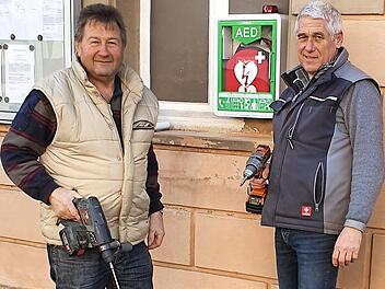 Die Vorsitzenden Rainer Schüll von der Feuerwehr (links) und Reinhold Klein vom Sportverein (rechts) brachten den Defibrillator am Haus der Vereine in Gemeinfeld an. Foto: privat