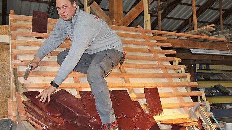 Um Prüfungssituationen zu simulieren, hat der angehende Dachdeckermeister Robert Domschke ein Dach im Maßstab 1:1 nachgebaut. Im Kehlbereich, dem Übergang zwischen zwei geneigten Dachflächen, befestigt er mit Hammer, Nagel und einem Edelstahldraht einen Ziegel. Foto: Stöckel